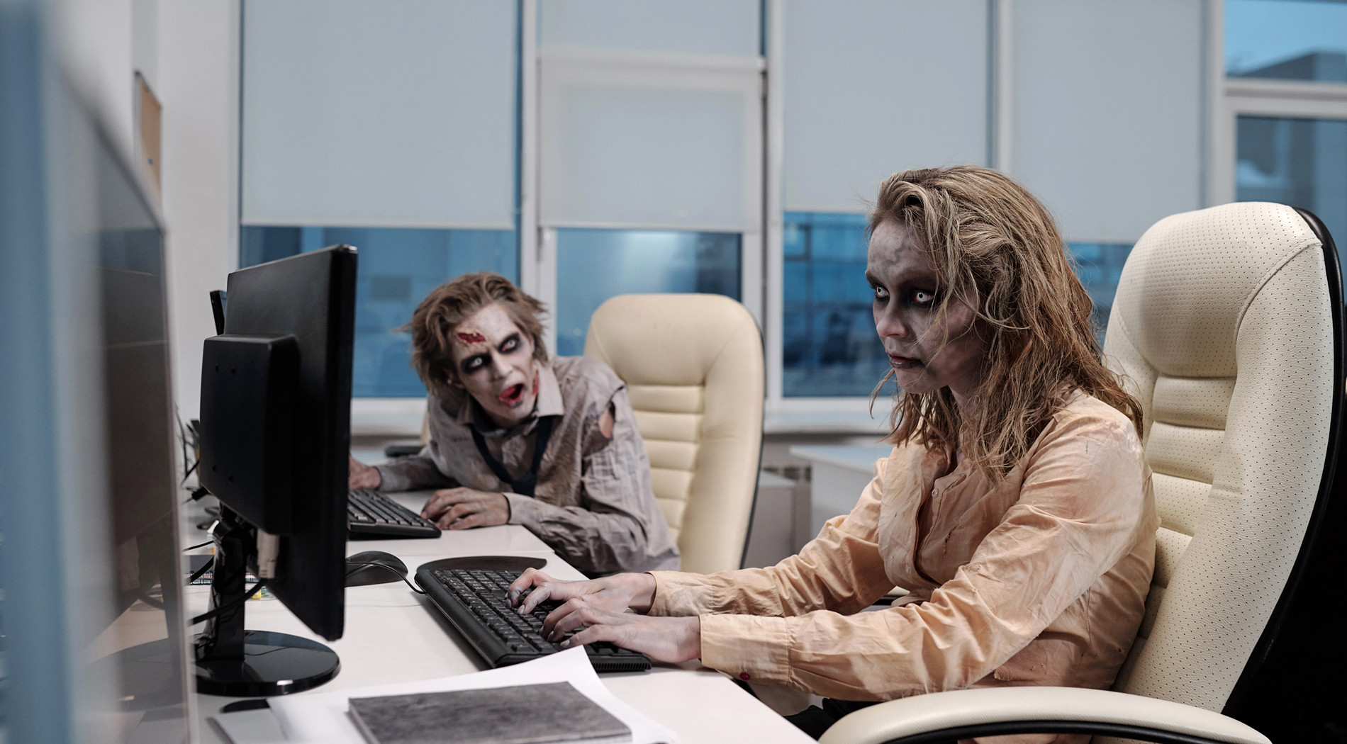 Due impiegati svolgono attività di routine in un ambiente di lavoro moderno, rappresentando un’organizzazione in modalità zombie — attiva nella forma, ma priva di vita nell’identità, nella collaborazione e nel rinnovamento creativo.